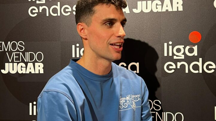 Carlos Alocén conversando en una rueda de prensa, con fondo del logo de la liga.