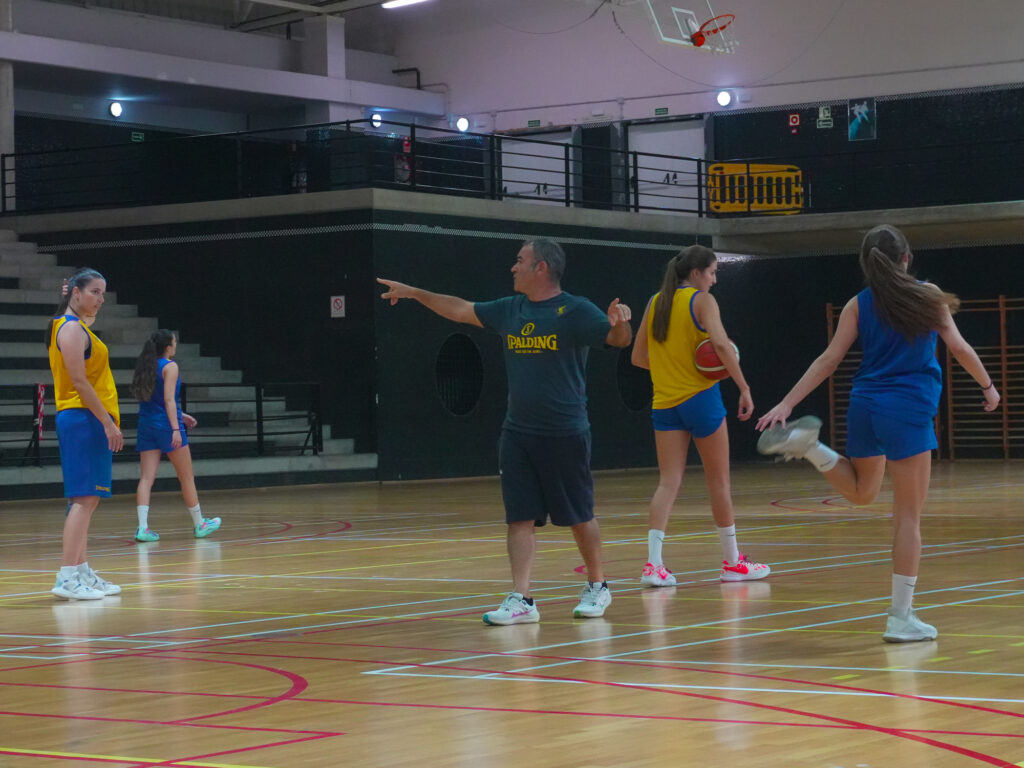 Entrenador dirige a jugadoras durante práctica de baloncesto en el gimnasio.