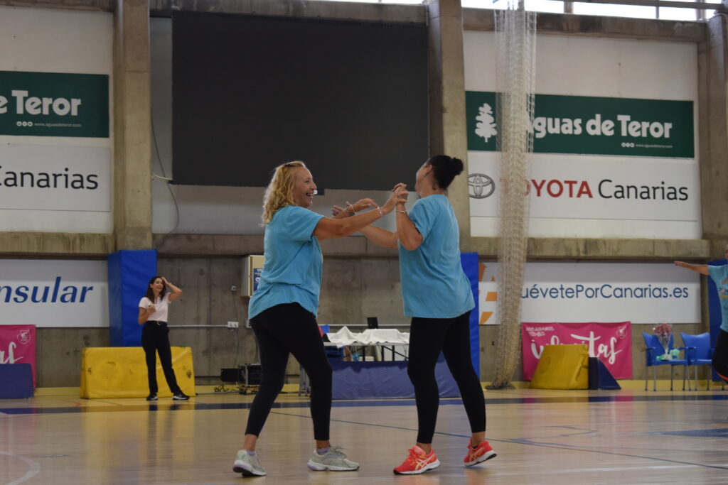 Dos mujeres sonrientes en camisetas azules disfrutan y se mueven en una cancha de baloncesto.