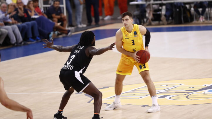 Dos jugadores de baloncesto en acción durante un partido, uno con balón en la mano.