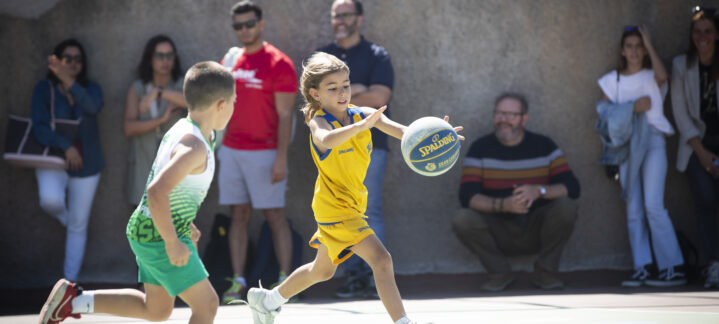 Niño corriendo con un balón de baloncesto mientras otro niño lo sigue en un campo.