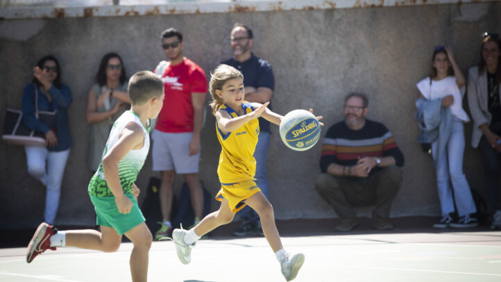 Niño corriendo con un balón de baloncesto mientras otro niño lo sigue en un campo.