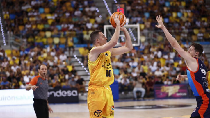 es una pista muy difícil""",Jugador de baloncesto lanzando a canasta con un árbitro y un rival cerca.