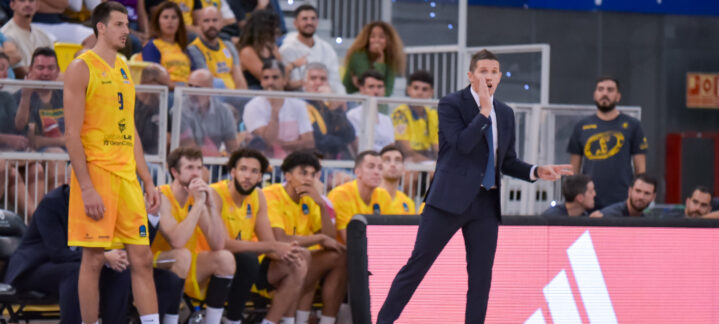 Entrenador Jaka Lakovic da instrucciones durante un partido, con jugadores en la banca.