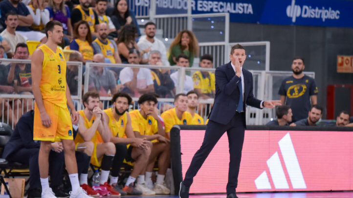 Entrenador Jaka Lakovic da instrucciones durante un partido, con jugadores en la banca.