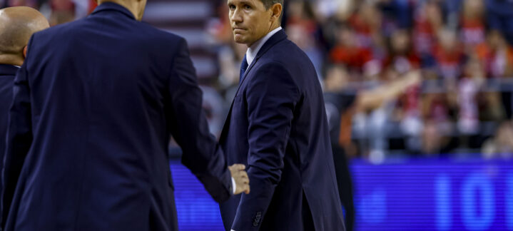 Entrenador Jaka Lakovic observa el partido con seriedad mientras habla con asistentes.