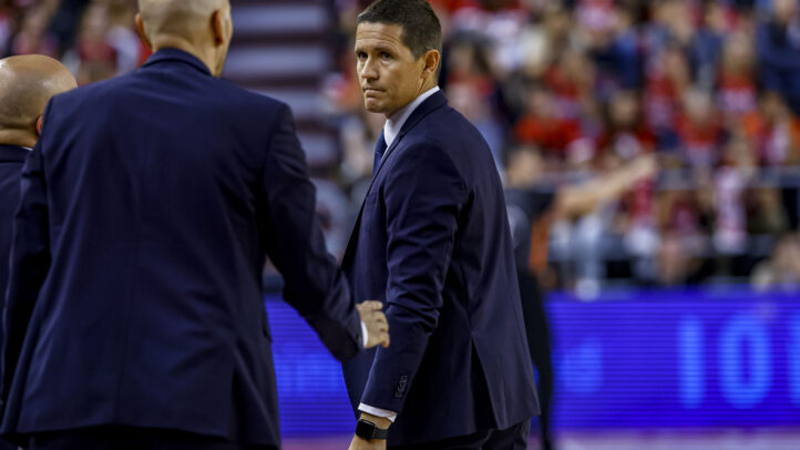 Entrenador Jaka Lakovic observa el partido con seriedad mientras habla con asistentes.