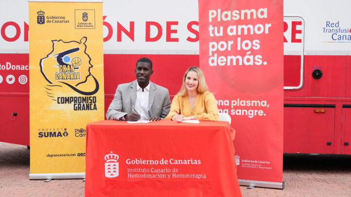 Dos personas firman un acuerdo en un evento de donación de sangre, junto a banners promocionales.