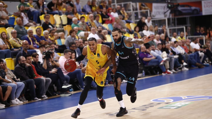 Jugador del Gran Canaria driblando mientras es seguido por un oponente en un partido.