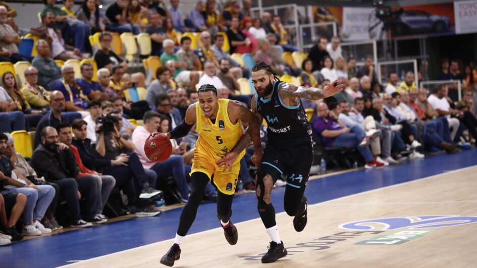 Jugador del Gran Canaria driblando mientras es seguido por un oponente en un partido.