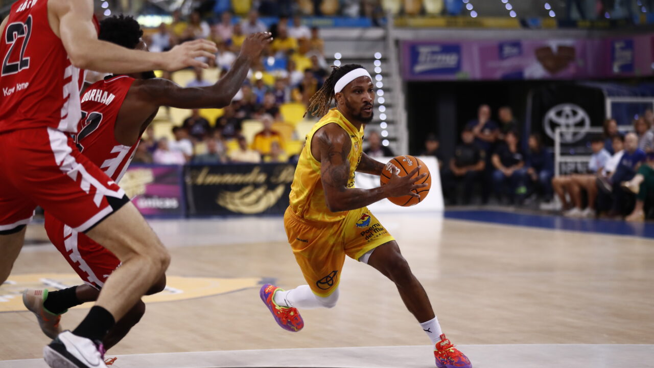 Jugador driblando con un balón de baloncesto, en acción durante un partido.