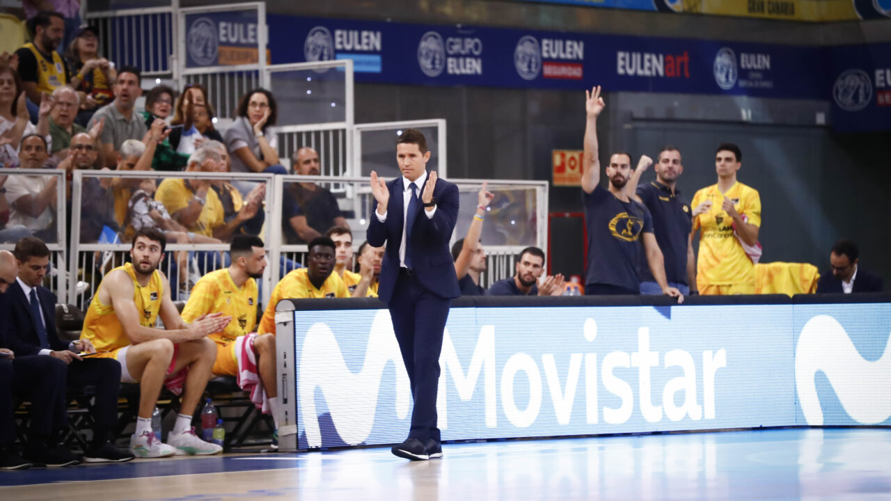 Entrenador aplaudiendo mientras el equipo está sentado en el banquillo durante un partido.