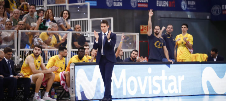 Entrenador aplaudiendo mientras el equipo está sentado en el banquillo durante un partido.