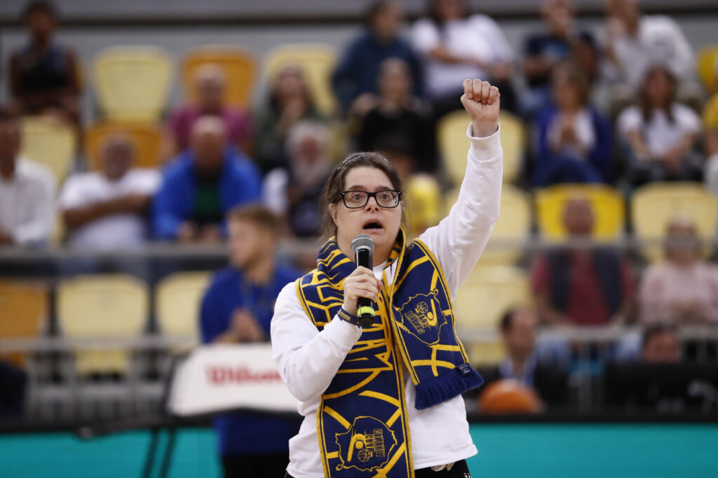 Mujer con micrófono y bufanda del Club Baloncesto Gran Canaria, animando al público.