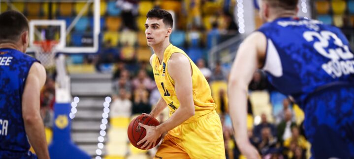 Jugador de baloncesto en acción con balón en una cancha, rodeado de adversarios.