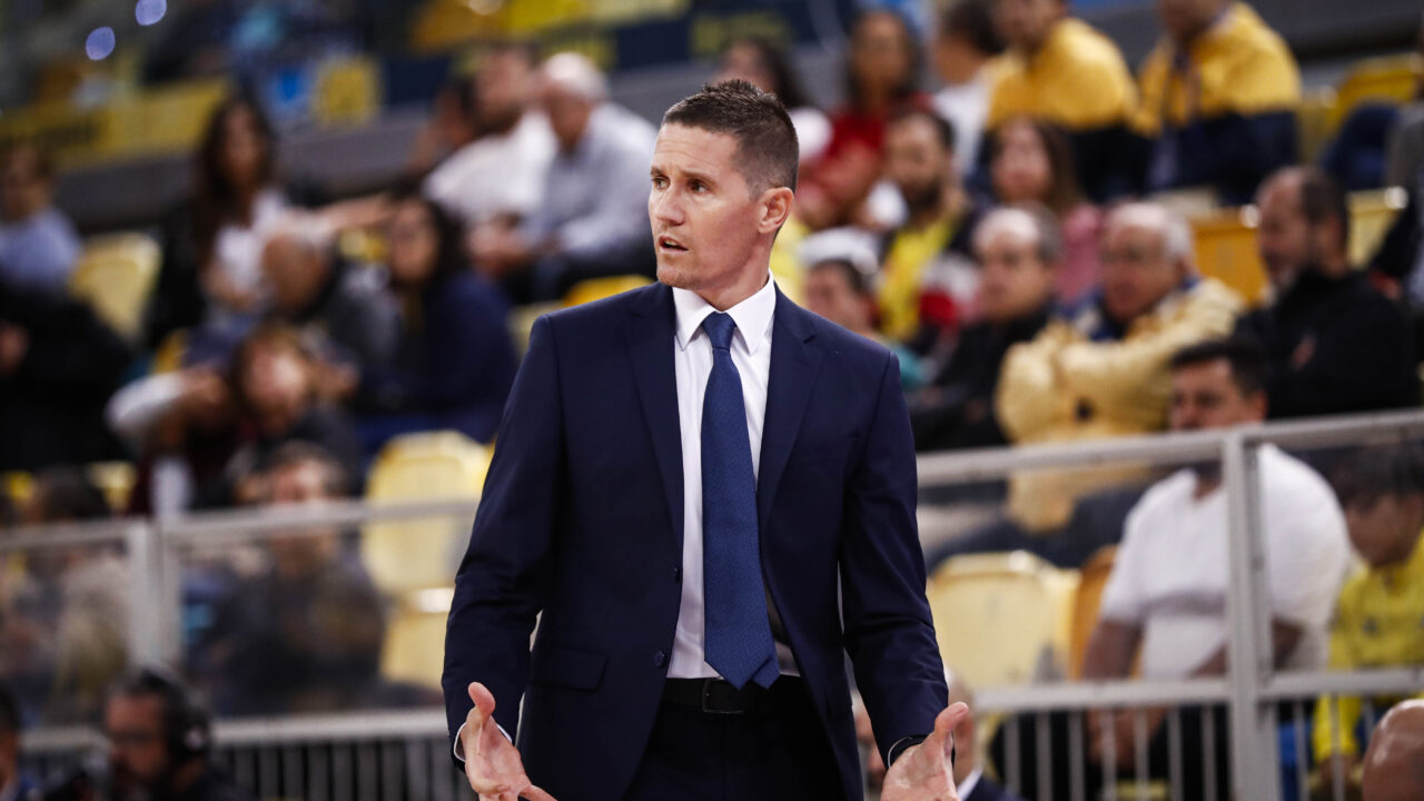 Entrenador gesticulando durante un partido con público en las gradas.