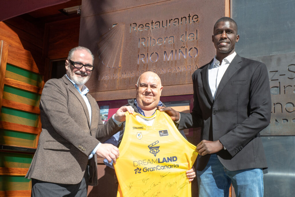 Tres hombres en un restaurante sostienen una camiseta del Club Baloncesto Gran Canaria.
