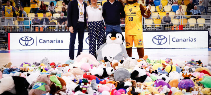 Tres personas posan junto a una gran cantidad de peluches en la pista de baloncesto.