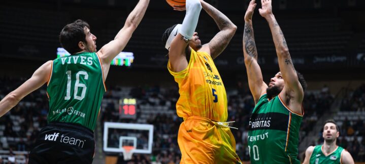 en diez claves",Jugador lanzando a canasta mientras es defendido por dos oponentes en un partido de baloncesto.