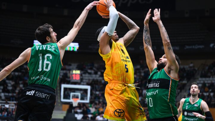 en diez claves",Jugador lanzando a canasta mientras es defendido por dos oponentes en un partido de baloncesto.