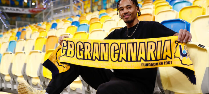 Jugador del CB Gran Canaria sostiene una bufanda del equipo en una tribuna vacía.