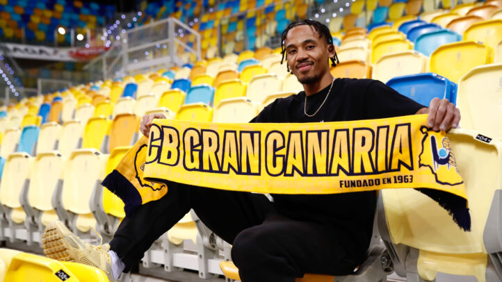 Jugador del CB Gran Canaria sostiene una bufanda del equipo en una tribuna vacía.