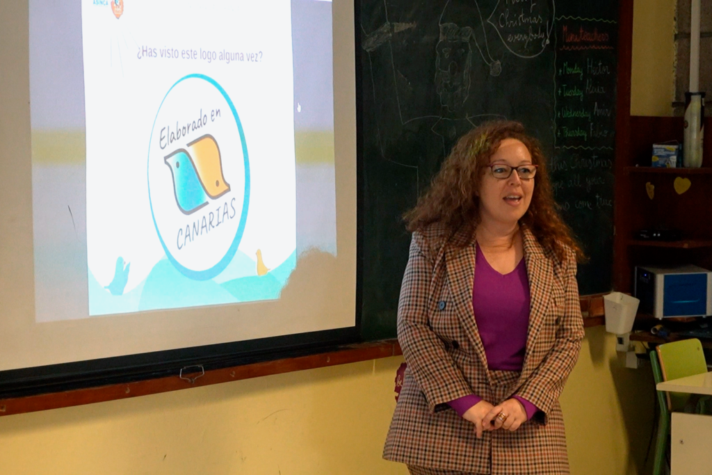 Mujer hablando frente a una pantalla con un logo de ""Elaborado en Canarias"".