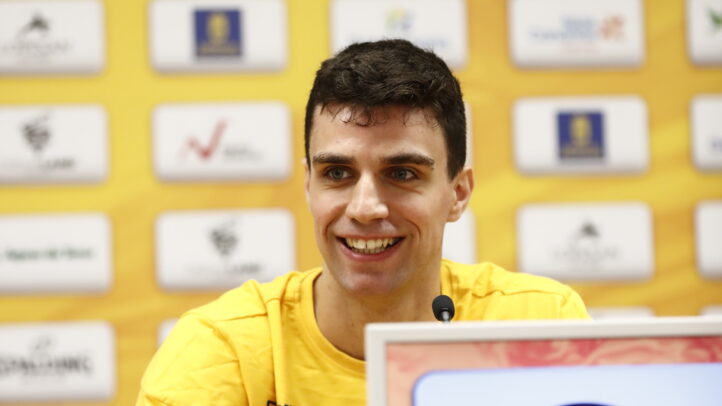 Jugador del CB Gran Canaria sonríe durante una rueda de prensa. Fondo amarillo con logotipos.