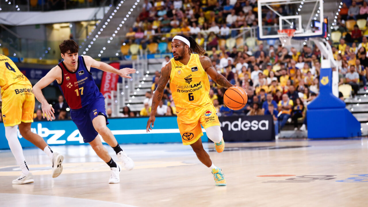 Jugadores de baloncesto en acción, con un atleta en amarillo avanzando con el balón.
