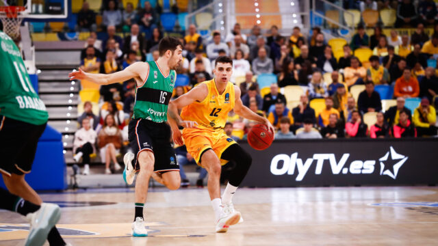 Jugadores en acción durante un partido de baloncesto con un público animado.