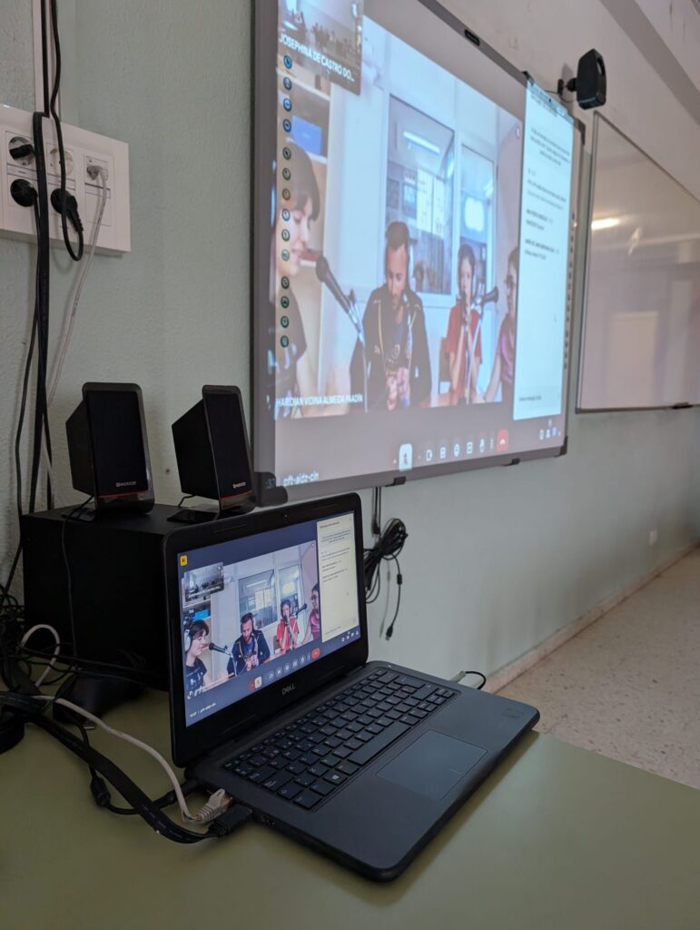 Pantalla proyectando videoconferencia con varias personas en un entorno educativo.