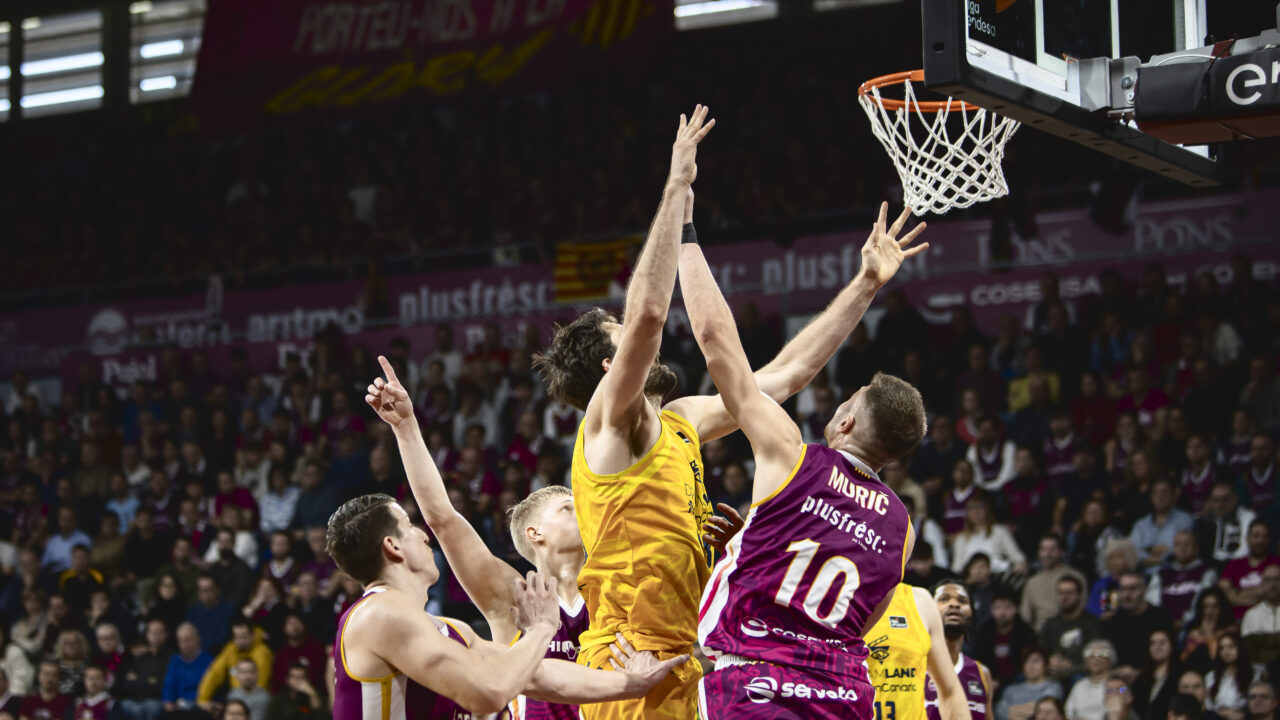 Jugadores luchando por el balón bajo el aro durante un partido de baloncesto.