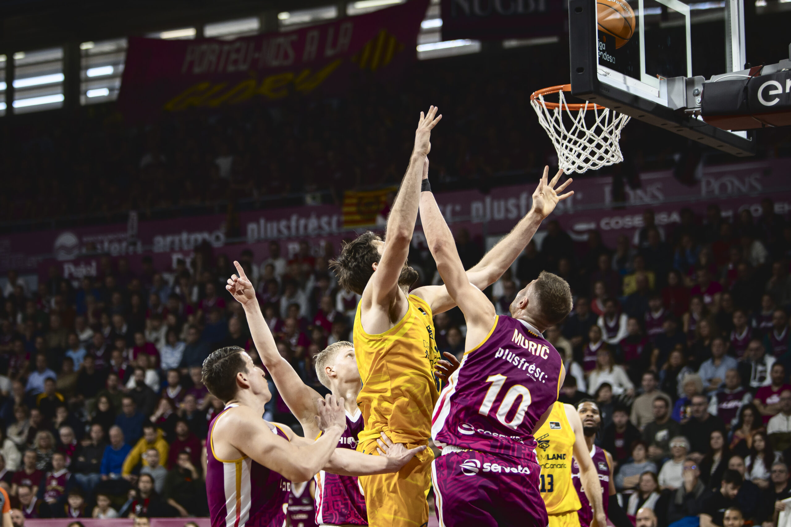 Jugadores luchando por el balón bajo el aro durante un partido de baloncesto.