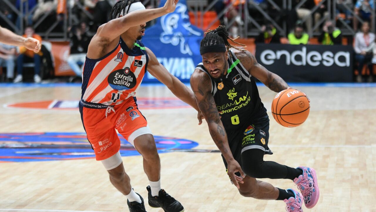 Jugador de baloncesto avanza con el balón mientras es defendido por un oponente.