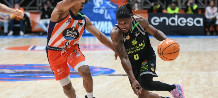 Jugador de baloncesto avanza con el balón mientras es defendido por un oponente.