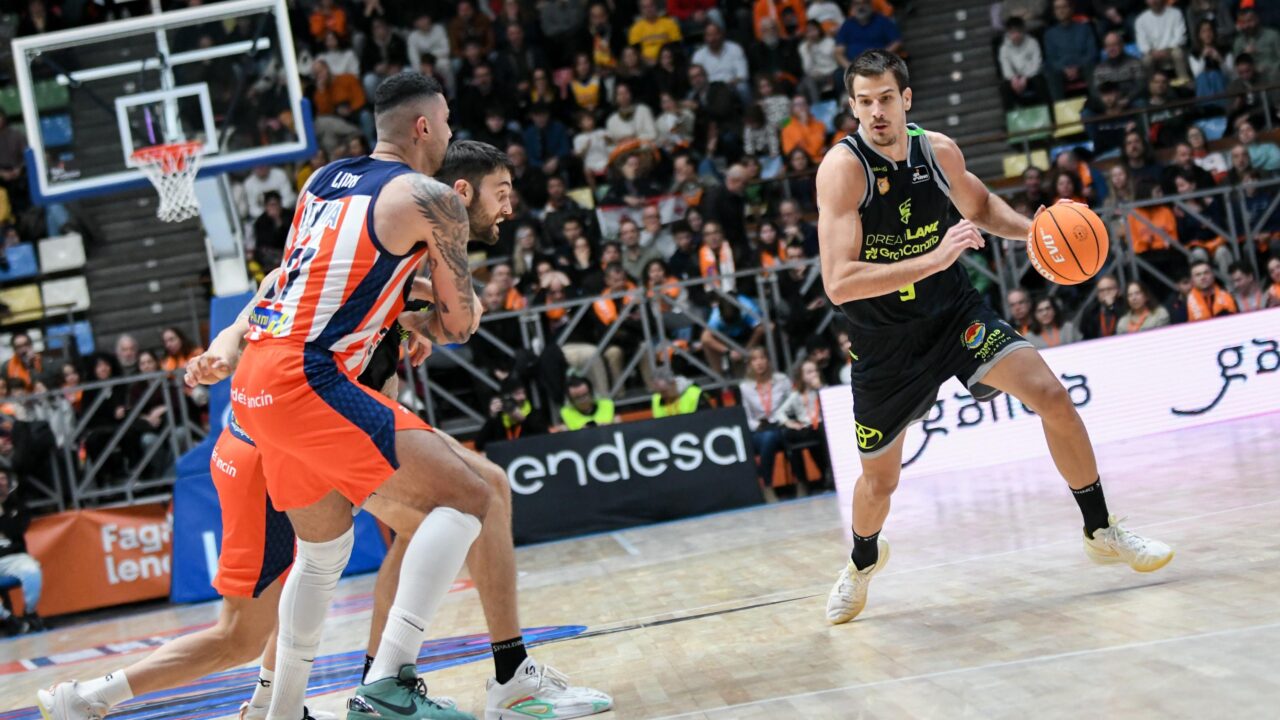 Jugadores en acción durante un partido de baloncesto, con un enfocado al jugador con balón.