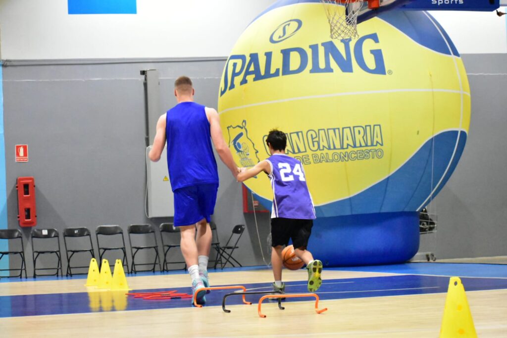 Entrenamiento de baloncesto, un jugador guía a un joven sobre una pista.