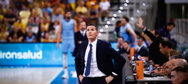 Entrenador observa el juego con preocupación en un partido de baloncesto.