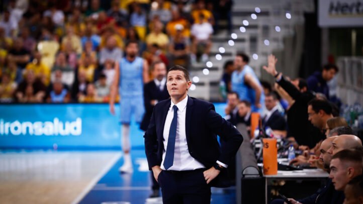 Entrenador observa el juego con preocupación en un partido de baloncesto.