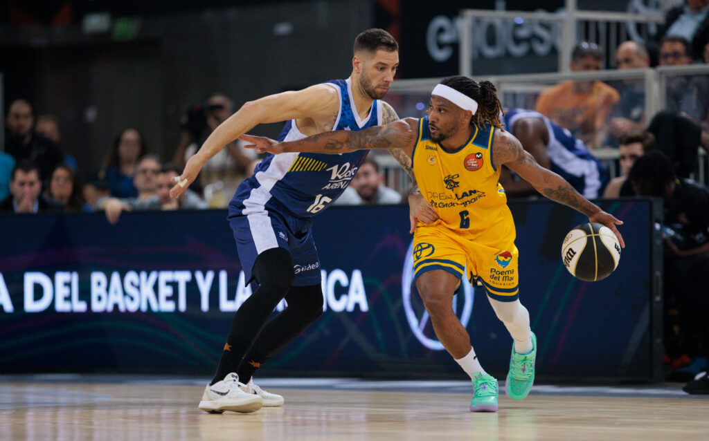Jugadores de baloncesto compiten en un partido, el jugador amarillo driblando el balón.