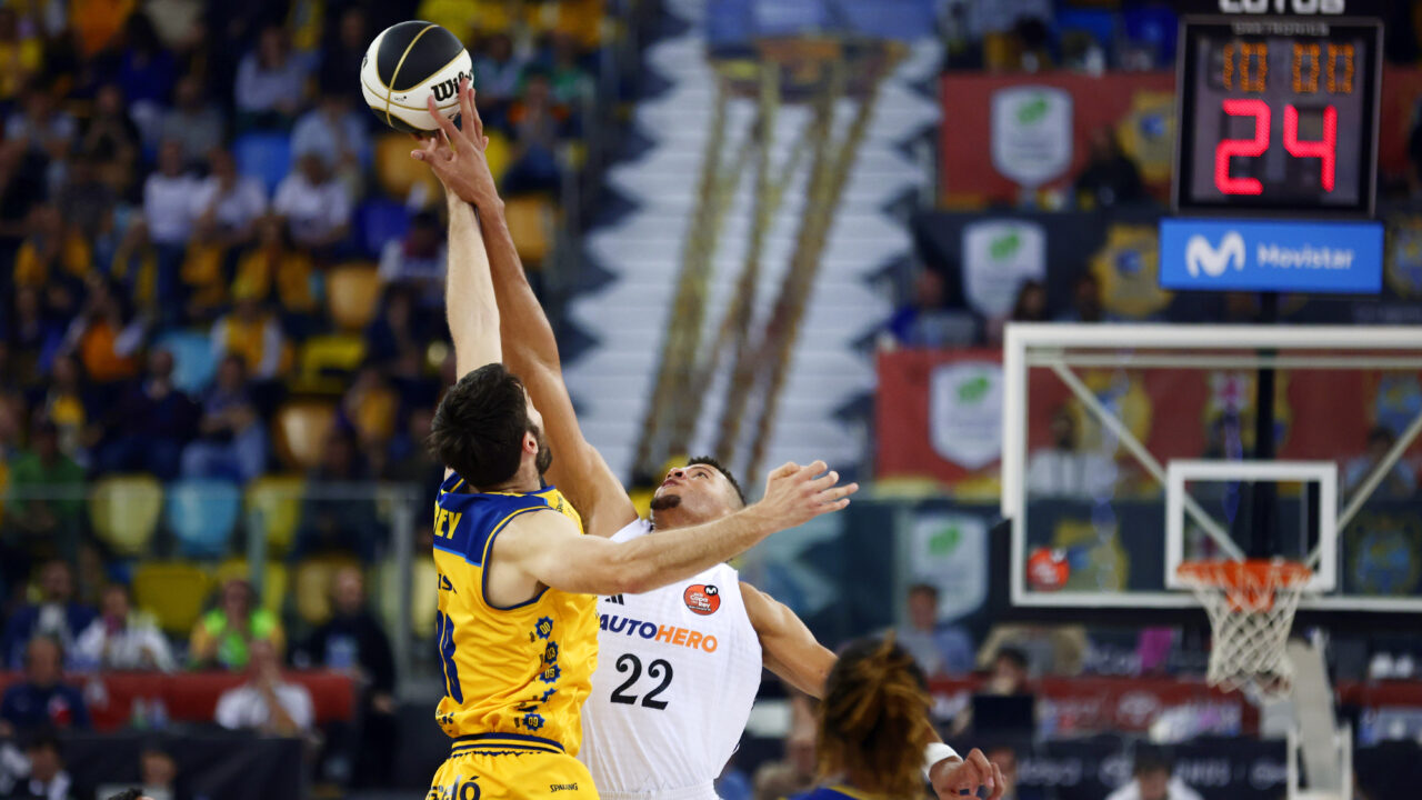 Dos jugadores de baloncesto saltan para capturar el balón en un partido.
