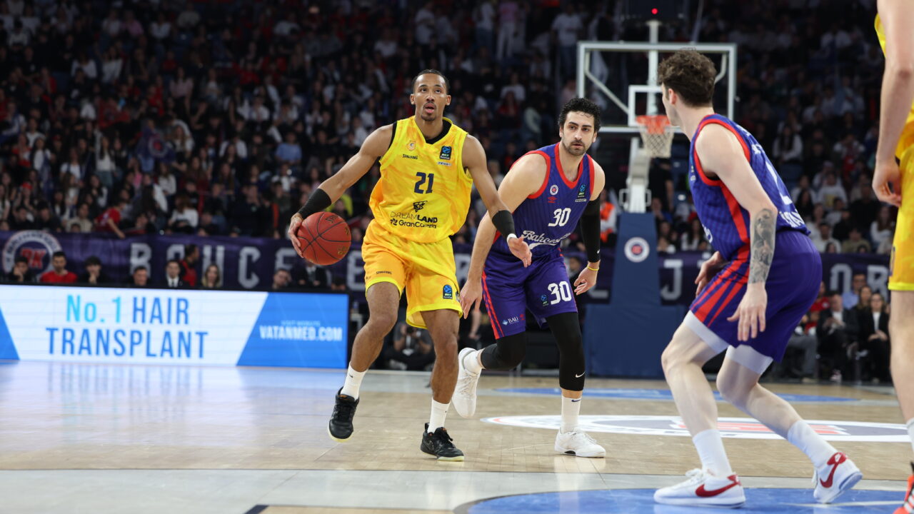 Jugadores de baloncesto en acción durante un partido decisivo con gran afluencia de público.
