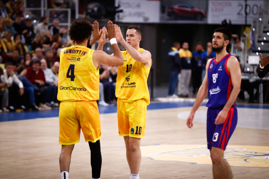 Dos jugadores del Gran Canaria celebran un punto, mientras un rival observa.