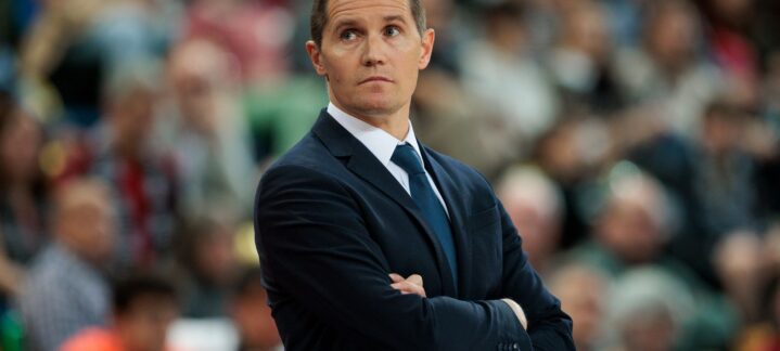 Entrenador del equipo observa el partido con atención, brazos cruzados, en un ambiente de competición.