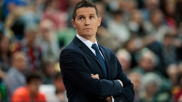 Entrenador del equipo observa el partido con atención, brazos cruzados, en un ambiente de competición.