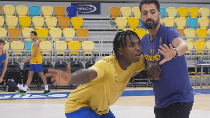 Entrenador instruye a un jugador de baloncesto en la cancha durante un entrenamiento.