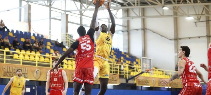 Jugador del equipo amarillo lanza a canasta mientras es defendido por un rival rojo.