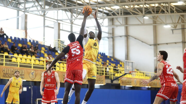 Jugador del equipo amarillo lanza a canasta mientras es defendido por un rival rojo.