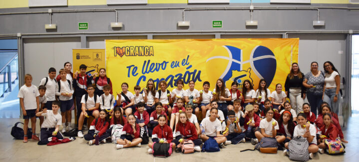 Grupo de jóvenes sonrientes en un evento del CB Gran Canaria, con una gran pancarta de fondo.
