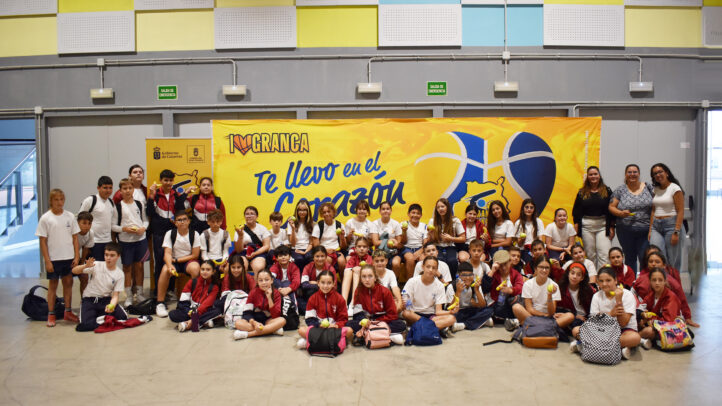 Grupo de jóvenes sonrientes en un evento del CB Gran Canaria, con una gran pancarta de fondo.